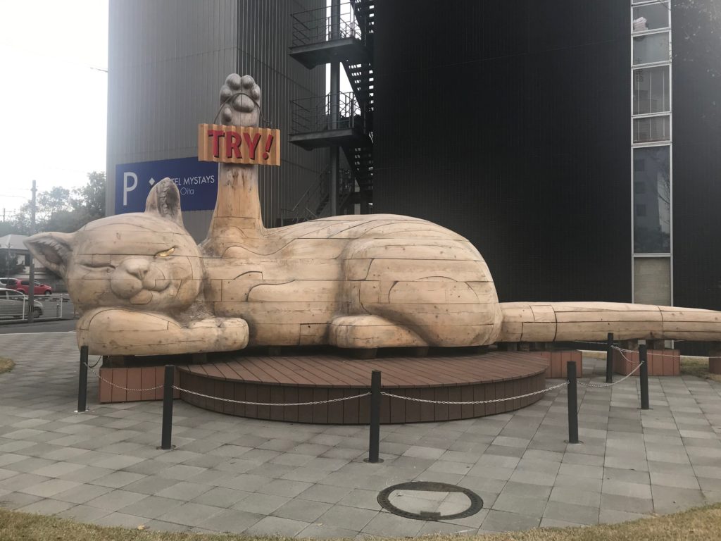 large sculpture of makineko cat with paw upraised holding sign that says "try!"